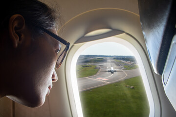 A young woman looks at the airport runway from a flying plane