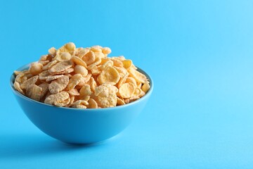 Bowl of tasty crispy corn flakes on light blue background, space for text