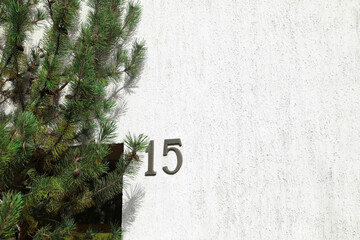 House number 15 on white textured wall outdoors. Space for text