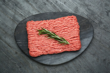 Raw fresh minced meat with rosemary on black wooden table, top view