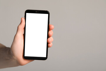 Man holding smartphone with blank screen on light grey background, closeup. Mockup for design