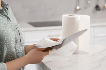 Woman wiping knife with paper towel at white marble table in kitchen, closeup