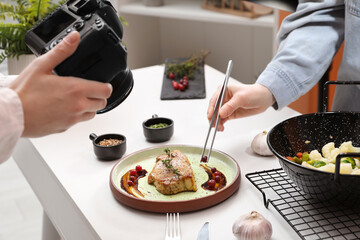 Professional photographer taking photo while food stylist decorating composition with meat medallion in studio, closeup