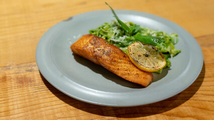 Grilled salmon and pasta served on a blue plate, placed on a wooden table.