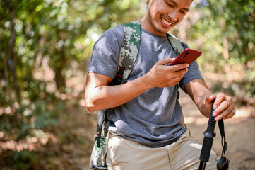 Cropped image of a happy Asian male traveler with trekking gear using his smartphone