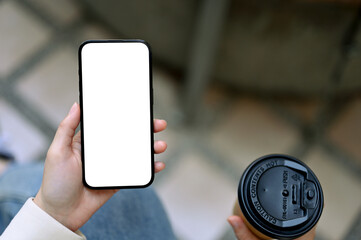 A woman sits at the coffee shop outdoor area, using her smartphone and sipping coffee