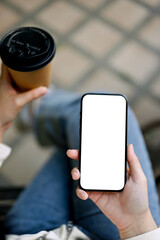 Top view image of a woman sipping coffee and using her smartphone at outdoor space.