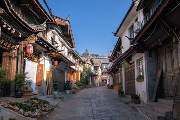 Fototapeta na wymiar LIJIANG, YUNNAN PROVINCE, CHINA - August, 2021: Scenic view of narrow street with souvenir shops in the Old Town of Lijiang. Beautiful wooden facades of traditional oriental Chinese houses.