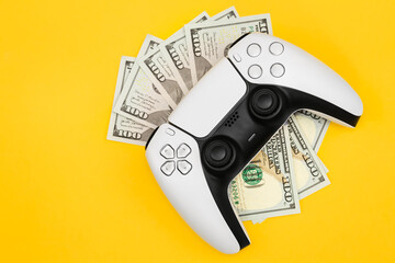 Modern gamepad and money on yellow background, top view, concept of gambling addiction.