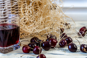 Cherry and cherry juice or wine on a wooden table, a decanter and a glass with juice, a basket with...
