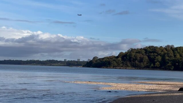 Plane flying over Dalmeny sunlit wild beach near Edinburgh Airport. Pan shot. Late afternoon sunlight