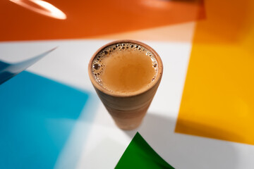 Hot, milky, spiced tea ('masala chai') served in a clay cup, against a multicolor backdrop.