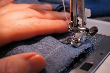 Sewing machine with fabric being sewn by needle and thread. A textile creative craft activity that creates clothing and interior furnishings.