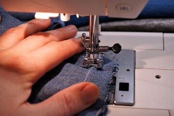 Sewing machine with fabric being sewn by needle and thread. A textile creative craft activity that creates clothing and interior furnishings.