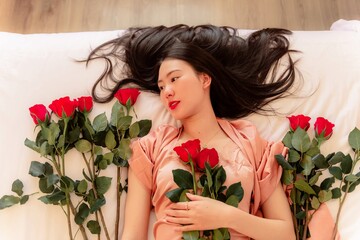 woman in pajamas colored rose gold With a red rose on the bed resting in the morning, Background concept, closeup flower.