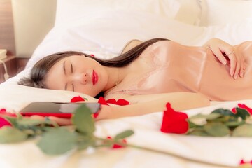 Obraz na płótnie Canvas woman in pajamas colored rose gold With a red rose on the bed resting in the morning, Background concept, closeup flower.