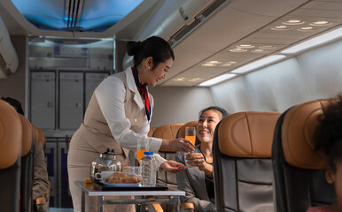Airplane flight attendant serving orange juice to female passenger in cabin. - 571784123