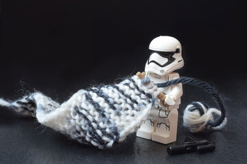 Fototapeta premium Lego minifigure of warrior Star Wars is knitting a long scarf with stocks. Editorial illustrative image of popular plastic constructor. Stop war concept image.