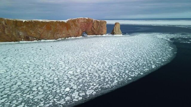 aerial view of Percé rock in the winter with ice on the ocean.