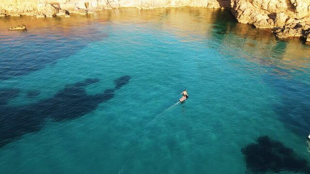 Aerial View Of Male Using Electric Surfboard Across Turquoise Waters Off Cala Escondida Coastline 