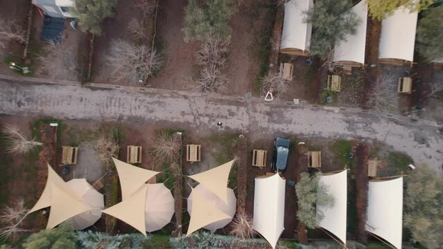 Top down descending aerial view camping canvas tent plot rows in autumn woodland