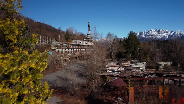 Aerial shot over Consonno ghost town in Italy, ruined building surrounded by green vegetation.