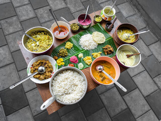 traditional south indian food platter with rice in a banana leaf and a variety of dishes arranged...