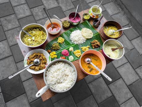 traditional south indian food platter with rice in a banana leaf and a variety of dishes arranged in a table