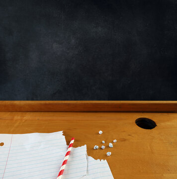 Spitballs, with red and white striped straw and paper on a vintage school desk top with copyspace on the blackboard