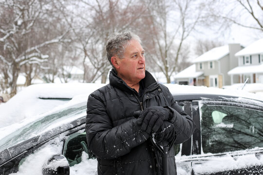 Man outside shoveling snow around his car in winter