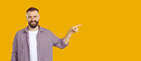 Your ad can be here. Portrait of smiling man pointing with his index finger at copy space on orange background. Caucasian man in casual clothes advertises and presents. Panoramic web banner.