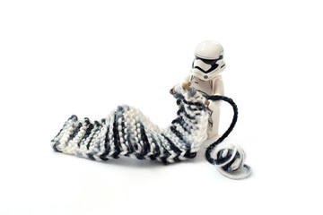 Naklejka premium Lego minifigure of warrior Star Wars is knitting a long scarf with stocks. Editorial illustrative image of popular plastic constructor. Stop war concept image.
