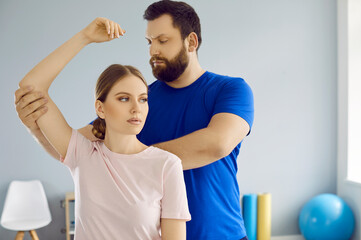 Fototapeta premium Osteopath masseur kneads joints of young woman's hands during treatment at rehabilitation center. Serious professional male doctor helps patient to recover from elbow injury. Concept of physiotherapy.