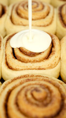 Pouring fluffy frosting on Freshly baked cinnamon rolls or Cinnabon close up