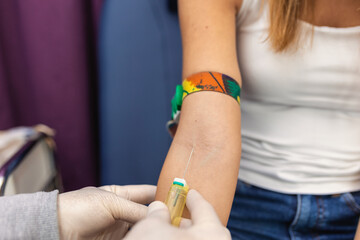 Preparation for blood test with pretty young woman by female doctor medical uniform on the table in white bright room. Nurse pierces the patient's arm vein with needle blank tube