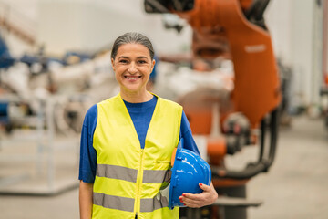 Caucasian mature woman engineer in robotic factory - female worker with helmet and reflective vest -