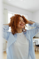 Vertical image of attractive happy cheerful student girl with red curly hair and sincere smile enjoying weekend morning at home dancing at kitchen, feeling carefree and relaxed, looking aside
