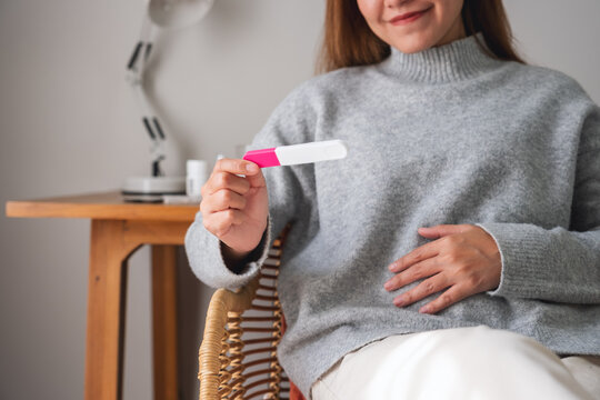 Closeup image of a happy woman touching her belly while checking a positive pregnancy test result