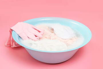 Wash basin with clothes and rubber gloves on pink background close-up, side view.