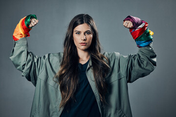 Woman, protest and rainbow fists for gay, LGBTQ or human rights against a gray studio background. Portrait of female activist standing ready in fighting flex for equality, empowerment or sexuality