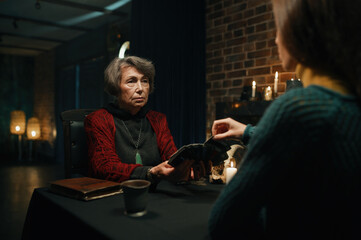 Old mature soothsayer holding divination tarot cards in front of client