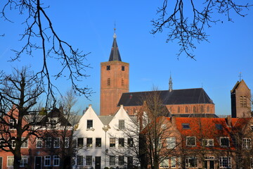 Fototapeta premium Historic houses located inside the fortified town of Naarden, Netherlands, with the clock tower of the Grote Kerk church in the background and Saint Vituskerk church on the right