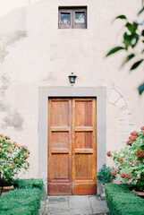 Fototapeta na wymiar Wooden door in the stone wall of an old villa among green flowering bushes