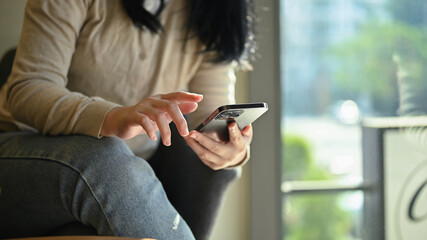 A young Asian woman relaxes in the coffee shop use g her smartphone at her table.