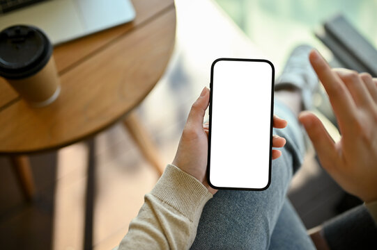 Top view image of a smartphone white screen mockup is in a woman's hand.