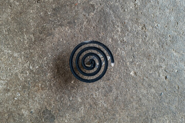 Burning black mosquito repellent coil on concrete floor background.