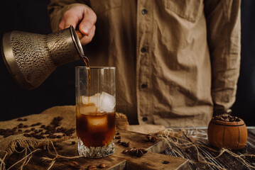 a male barista pours coffee from a metal mug into a glass with ice 4