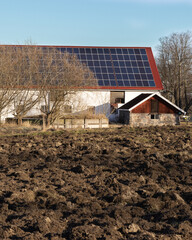 A large barn with solar cells on the roof and a small outbuilding with a stone foundation