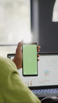 Vertical video: Female manager looking at greenscreen display in office, working with isolated mockup template on mobile phone. Young employee using blank copyspace mockup in coworking space.