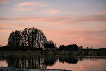 beautiful colorful evening sunset light landscape with house between trees on Lielupe river bank. Reflection in smooth calm mirror water surface